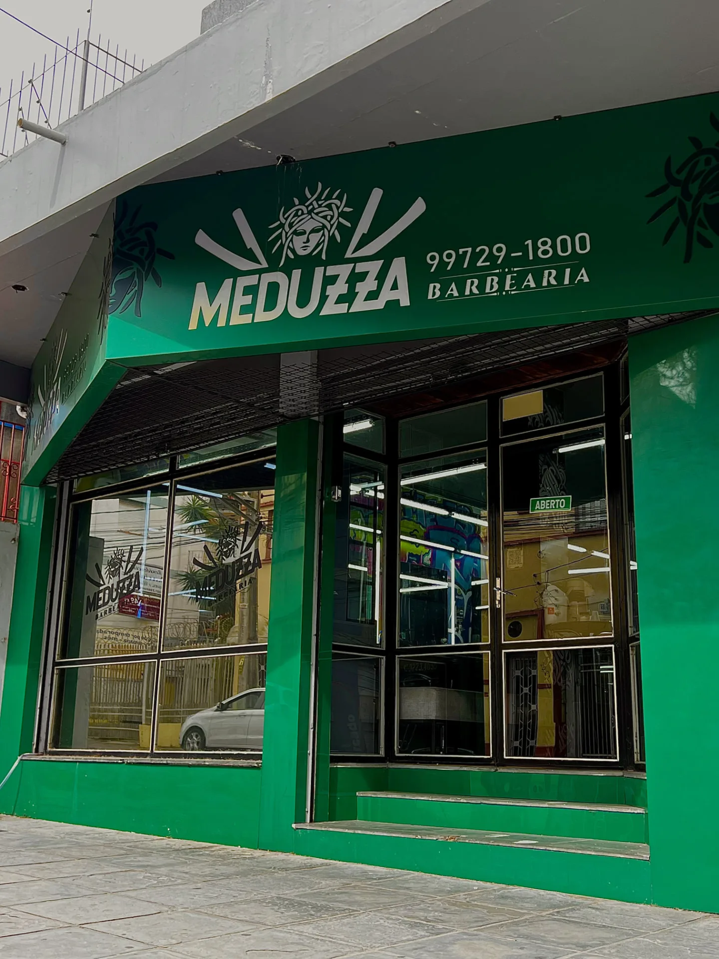 Fachada verde da Meduzza Barbearia com a placa da marca e a entrada envidraçada