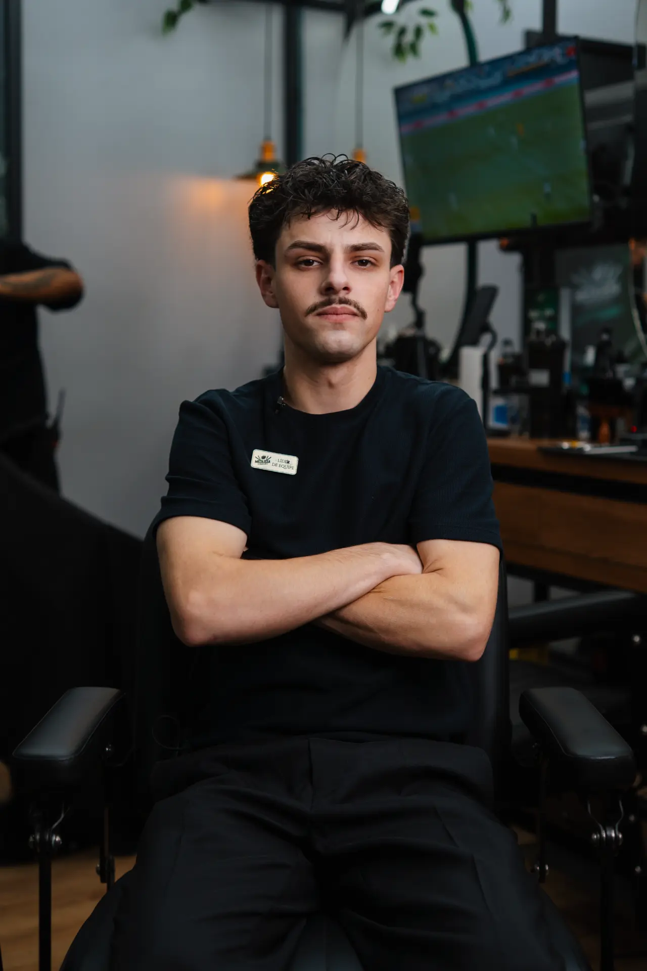 Barbeiro da Meduzza sentado em uma cadeira da barbearia, com os braços cruzados.